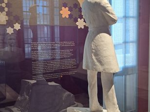 Maquette de monument représentant Julien Viaud, alias Pierre Loti, en uniforme de marin, de dos, sur un socle orné de bas-reliefs, exposée devant un portrait photographique de profil de l’écrivain au musée national de la Marine à Rochefort.
