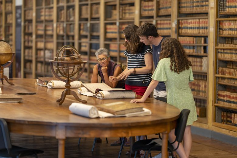 groupe regardant des ouvrages ancien déployés sur une table en bois 